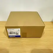 Omron C200HW-PA204S — brown Omron-branded carton with the C200HW-PA204 type label, lot number 2843YK, and barcode on a wooden tabletop
