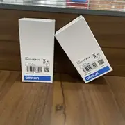 Omron C500-CE404 — two white Omron-branded boxes with the C500-CE404 type label and lot number 03325K on a wooden surface in front of a glass display shelf