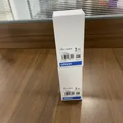 Omron C500-CE404 — one white Omron-branded box with the C500-CE404 type label, lot number 03325K, and barcode standing on a wooden surface with a glass display shelf behind it