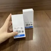 Omron C500-CE404 — a hand holding the C500-CE404 box showing the type label, lot number 03325K, and barcode on the front of the white box with a wooden surface behind