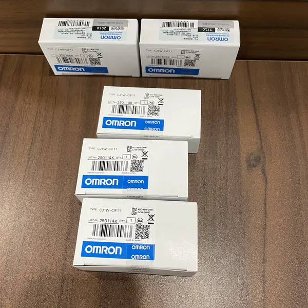 Omron CJ1W-CIF11 — five small white Omron-branded product boxes arranged on a wooden surface, each with the white CJ1W-CIF11 type label, the RS-422A ADAPTER Ver. 1.2 subtext, the KCC-REM-OMR-CJ1W-00061 KC mark, and the blue-and-white OMRON band along the bottom