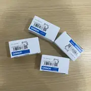 Omron CJ1W-CIF11 — four small white Omron-branded product boxes scattered on a wooden surface, each with the CJ1W-CIF11 type label, lots 241128K / 241225K, the KCC-REM-OMR-CJ1W-00081 KC mark, the KC logo, the crossed-bin disposal mark, and the blue-and-white OMRON band