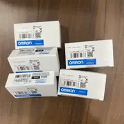 Omron CJ1W-CIF11 — six small white Omron-branded product boxes clustered on a wooden surface with several boxes showing the CJ1W-CIF11 type label / lot number / barcode / KC mark / blue-and-white OMRON band, one box turned to show the side panel RS-422A ADAPTER Ver. 1.2 subtext