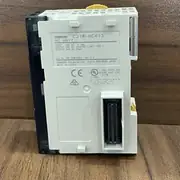 Omron CJ1W-NC413 — nameplate-side view of the module on a wooden surface showing the white label OMRON CJ1W-NC413 NC UNIT / INPUT: 24V DC 4.1mA / OUTPUT: 24V DC 16mA (W/ LIMIT RES.) / OUTPUT: 24V DC 30mA / Lot No. 180120M 0002 Ver. 2.3 / OMRON Corporation Kyoto. 600-8530 JAPAN / MADE IN CHINA / CE / cUL / IND. CONT. EQ. US FOR HAZ. LOC. 7ITM / Cl. I, DIV. 2, Gp. A, B, C, D / Cl. I, Zn. 2, Gp. IIC / Temp. Code T4 / CN2 Fujitsu header on the right edge