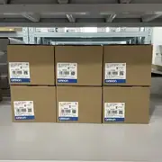 Six sealed Omron retail boxes of the CJ1W-PA205R stacked on a warehouse shelf, each labelled TYPE CJ1W-PA205R POWER SUPPLY UNIT with the blue OMRON logo