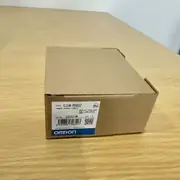 Omron CJ1W-PD022 — same brown cardboard box at a higher angle showing the top flaps, the CJ1W-PD022 type label on the front face, and the OMRON wordmark with the blue/white band at the bottom on a wooden table
