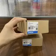 Omron CJ1W-SCU22 — second angle of the small retail wrapper showing the CJ1W-SCU22 type code, lot number, KC mark, and blue-and-white OMRON band on a wooden surface