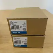 Omron CJ1W-SCU32 — two brown Omron cardboard boxes stacked on a wooden surface, each showing TYPE CJ1W-SCU32 / Ver.2.1 / LOT No. 230819M / QTY 1 / KCC-REM-OMR-CJ1W-00038 / barcode / OMRON Corporation / MADE IN JAPAN / blue OMRON band