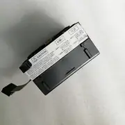 Omron CP1W-DA021 — angled top view of the black plastic CP1W Special I/O module on a grey surface showing the side-mounted CAUTION label with bilingual (English / Japanese) wiring instructions, the dark plastic housing, and the small expansion connector visible at the bottom