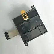Omron CP1W-DA021 — flat cable and terminal block side view of the CP1W module on a grey surface showing the 16-pin grey flat expansion cable on the left and the yellow plastic DIN-rail / release tab at the top of the housing