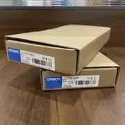 Omron CS1W-CN223 I/O connecting cable — installed between a CS1H CPU rack and a CS1W-BC083 expansion rack in a control cabinet, with both ends connected and the cable routed through the cabinet cable channel