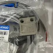 Omron D4C-1201 limit switch — close-up of the metallic switch body in plastic bag showing the side label D4C-1201 BLACK COM NO White NC, AC-15 2A/250V, DC-13 2A/30V, IP67, MADE IN JAPAN, with Omron authenticity card showing QR code