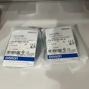 Omron E2B-M12KN05-WZ-B1 M12 inductive sensor — installed in a pneumatic cylinder's end-of-stroke position, detecting the ferrous piston ring through the cylinder body's aluminum wall, with the 2 m PVC cable returning to a CP1W-ID211 digital input module