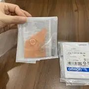 Omron E2B-S08KS02-MC-B1 inductive sensor — three sealed bags on wood with orange-tinted plastic mounting nuts visible through the transparent window of the leftmost bag