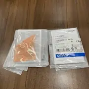 Omron E2B-S08KS02-MC-B1 inductive sensor — two sealed Omron-branded plastic bags with stainless steel M8 threaded sensor bodies inside and instruction sheets visible