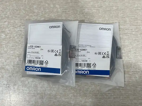 Omron E2E-X2ME1 inductive proximity sensor -- M8 threaded barrel with 8 mm hex flats, brass nickel-plated body, sensing face on the front with yellow operation LED, 2 m oil-resistant PVC cable exiting axially from the rear.