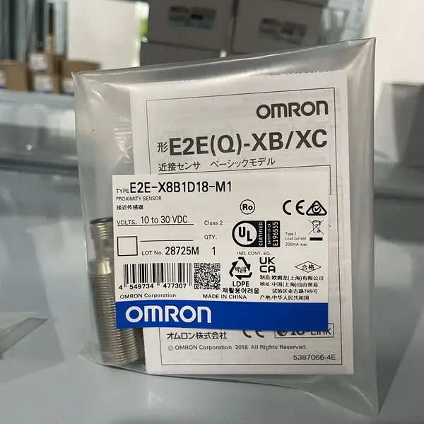 Omron E2E-X8B1D18-M1 — front view of the M18 shielded inductive sensor showing the PBT active face, the brass / stainless barrel, and the two lock nuts on the threaded body