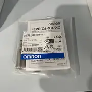 Omron E2E-X8B1D18-M1 installed in a metal bracket flush against a steel target plate with an XS2F-M12 patch cord trailing to the panel