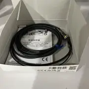 Omron E2EC-C1R5D1 — the 5.4 mm brass sensing head with the 0.4 m cable exiting the rear and the inline amplifier downstream with its operation LED