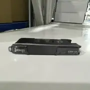 Omron E3NX-CA6 — top-down view of the slim black E3NX-CA6 fiber amplifier showing the OMRON wordmark on the top, the E3NX-CA MODEL IND label on the right side, the fiber input port on the left, and the clear plastic cover on the top face on a white surface