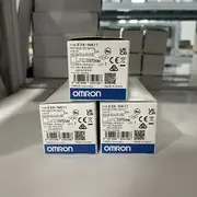 Omron E3X-NA11 2M paired with an E32-D12 diffuse-reflective fiber optic cable mounted 15 mm above a vibratory feeder bowl detecting small plastic parts - the 5-level LED bar shows 3 green LEDs (stable excess gain) and the operation indicator (orange) lights when a part passes under the fiber