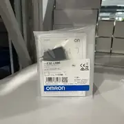 Omron E3Z-LR86 installed aimed across a packaging conveyor at an E39-R1 reflector mounted opposite, triggering reliably on a small part while ignoring the shiny-foil label on the package
