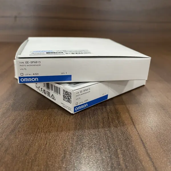 Omron EE-SPX613 — pair of white Omron cardboard boxes stacked on a wooden surface, each labelled TYPE EE-SPX613 PHOTO MICROSENSOR with the OMRON wordmark, lot A32t, CE / EAC marks, and barcode
