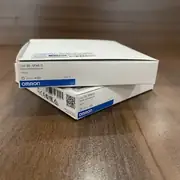 Omron EE-SPX613 — pair of white Omron cardboard boxes stacked on a wooden surface, each labelled TYPE EE-SPX613 PHOTO MICROSENSOR with the OMRON wordmark, lot A32t, CE / EAC marks, and barcode