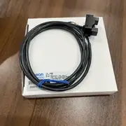 Omron EE-SPX613 — black plastic fork-shaped photomicrosensor body on top of the white Omron box, with the pre-wired 1 m oil-resistant cable (4 conductors with brown / blue / black / white) coiled and tied with a blue cable tie