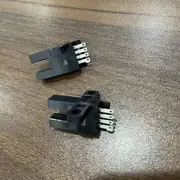 Omron EE-SX672 slot sensor — two units on a desk showing the T-shaped profile from the side and the 4-pin connector pins at the rear