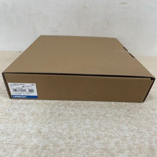 Omron NB10W-TW01B HMI — brown cardboard shipping box on the floor with Omron label TYPE NB10W-TW01B VER 1.1, LOT 05924M, QTY 1, OMRON Corporation, MADE IN CHINA, and Chinese-language shipping markings