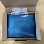 Omron NB10W-TW01B HMI — open shipping box showing the 10.1-inch HMI unit inside a blue anti-static bag with POWER LED visible at the top, multilingual programming precautions and safety instructions included, OMRON logo visible in the bottom right corner