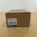 Omron NB3Q-TW01B-V1 — brown Omron-branded product box with the white NB3Q-TW01B type label, the OMRON Corporation wordmark on the blue-and-white band at the bottom, the barcode label, and the Omron Kyoto Japan address on a wooden surface