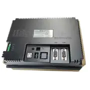 Omron NB7W-TW00B — back face of the same HMI installed in a brown cardboard tray, with the NB7W-TW00B INTERACTIVE DISPLAY type label, lot 26714M, Ver. 1.1, KCC-REM-OMR-NC-00483 KC mark, COM1 Output 5V DC 250mA rating, MADE IN CHINA, and the same SW1 / SW2 DIP, MODE, and connector layout visible above