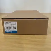 Omron NB7W-TW00B — second angle of the open inner product box in the outer sleeve, showing the NB7W-TW00B / PROGRAMMABLE TERMINAL label, KCC mark, and blue-and-white OMRON band on a wooden surface