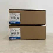 Omron NB7W-TW01B-V1 — two brown Omron-branded product boxes stacked on a wooden surface, the upper box with lot No. 18125M and the KCC-REM-OMR-NB-00013 KC mark, the lower box with the same NB7W-TW01B-V1 type label and the blue-and-white OMRON band