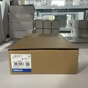 Omron NB7W-TW11B — single brown cardboard shipping carton on a metal storage shelf with the TYPE NB7W-TW11B / 可编程控制终端 / VER. 1.1 / KCC-REM-OMR-NB-00002 KC mark / lot 07320M / barcode / OMRON Corporation / MADE IN CHINA / blue OMRON band
