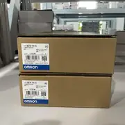 Omron NB7W-TW11B — two brown cardboard boxes stacked on a warehouse shelf (lots 11420M / 07320M), each showing TYPE NB7W-TW11B / 可编程控制终端 / VER. 1.1 / KCC-REM-OMR-NB-00002 KC mark / OMRON Corporation / MADE IN CHINA / blue OMRON band