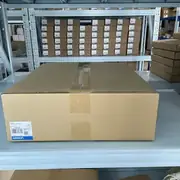 Omron NS12-TS01-V2 NS-series HMI — two stacked sealed retail boxes on warehouse shelves showing QTY 1 markings and Omron Corporation branding