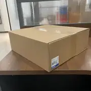 Omron NS12-TS01-V2 NS-series HMI — sealed shipping box showing TYPE NS12-TS01-V2 label and tape-sealed top for transit
