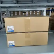 Omron NS12-TS01-V2 NS-series HMI — two boxed units on metal shelving showing QTY 1 labels and date-code markings on the retail packaging