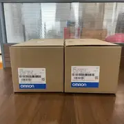 Omron R88M-1M75030H-S2 servo motor — two brown shipping boxes on the floor with detailed Omron labels showing TYPE R88M-1M75030H-S2, AC SERVO MOTOR, SER. NO. 03251701154P and 03251701241P, QTY 1, OMRON Corporation, MADE IN THE PHILIPPINES, OMRON blue band