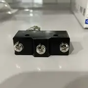 Omron Z-15GQ22-B basic switch — installed on a CNC machine-tool door interlock; the panel-mount body fits through the door frame with the M12 hex-nut securing it, the roller plunger rides against the door panel, NC contact cuts the 24 VDC spindle-drive enable signal when the door opens